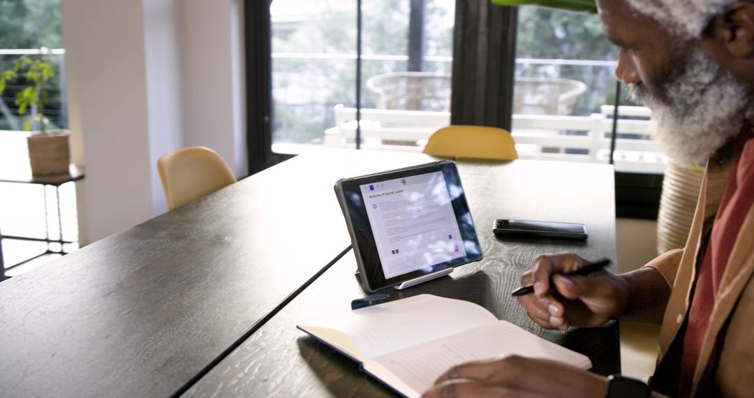 Senior Man Writing Notes in Home Office with Tablet