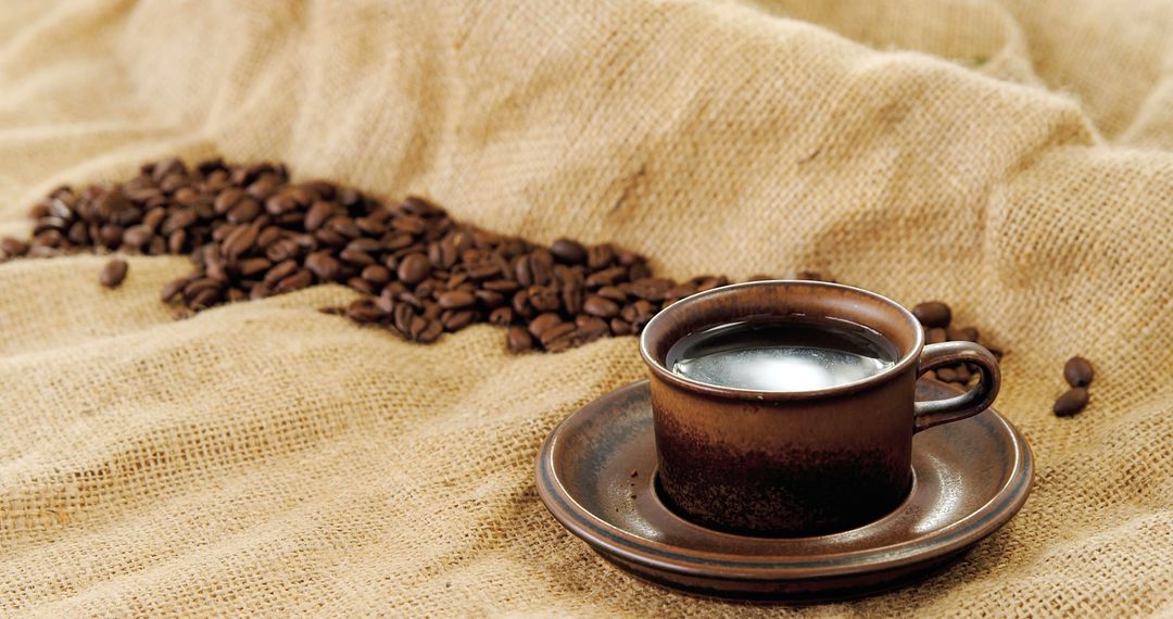 A steaming cup of coffee sits beside a trail of coffee beans on a burlap surface, with copy space - Free Images, Stock Photos and Pictures on Pikwizard.com