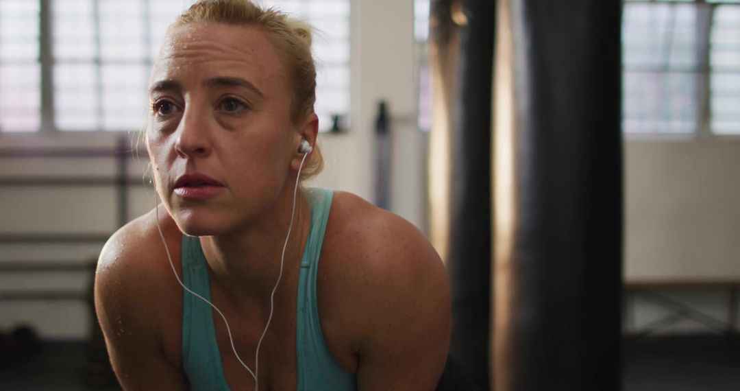 Determined Woman Taking Break in Boxing Gym with Earbuds