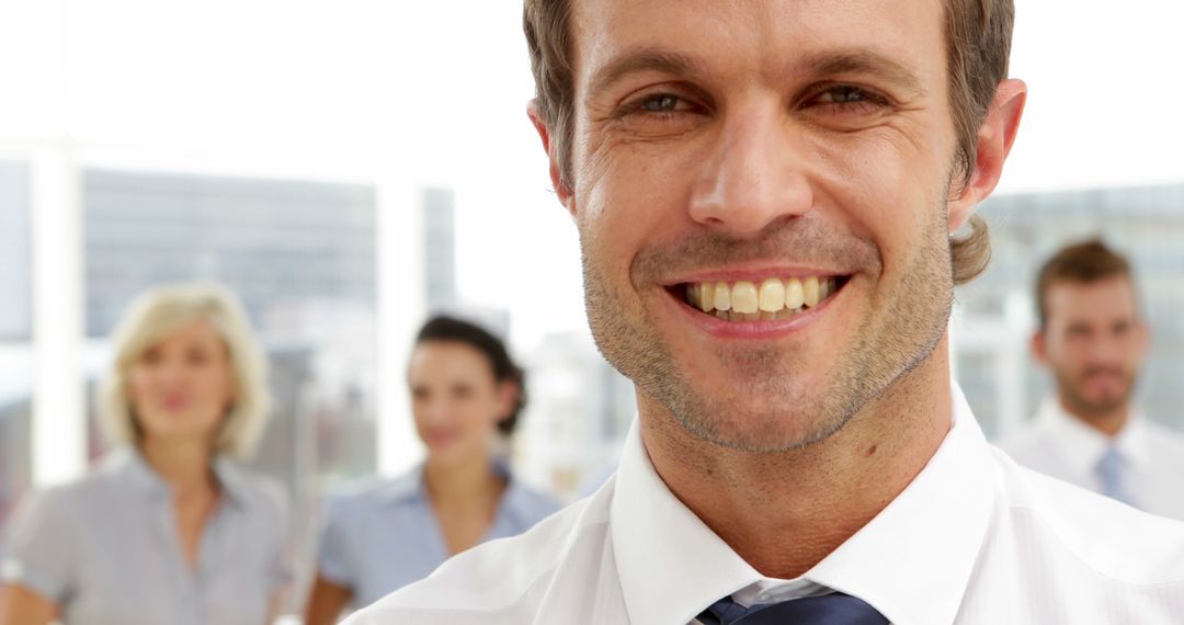 Confident Businessman Smiling in Office with Colleagues in Background - Free Images, Stock Photos and Pictures on Pikwizard.com