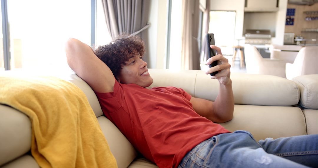 Young Man Relaxing on Sofa Holding Smartphone at Home