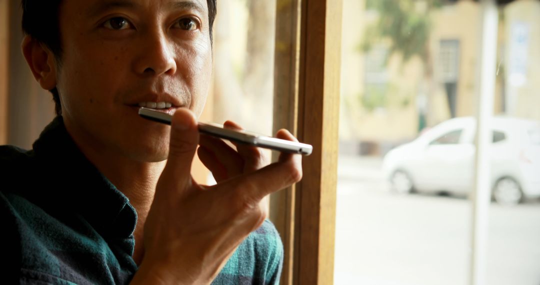 Man Using Smartphone Voice Command Feature Indoors by Window - Free Images, Stock Photos and Pictures on Pikwizard.com