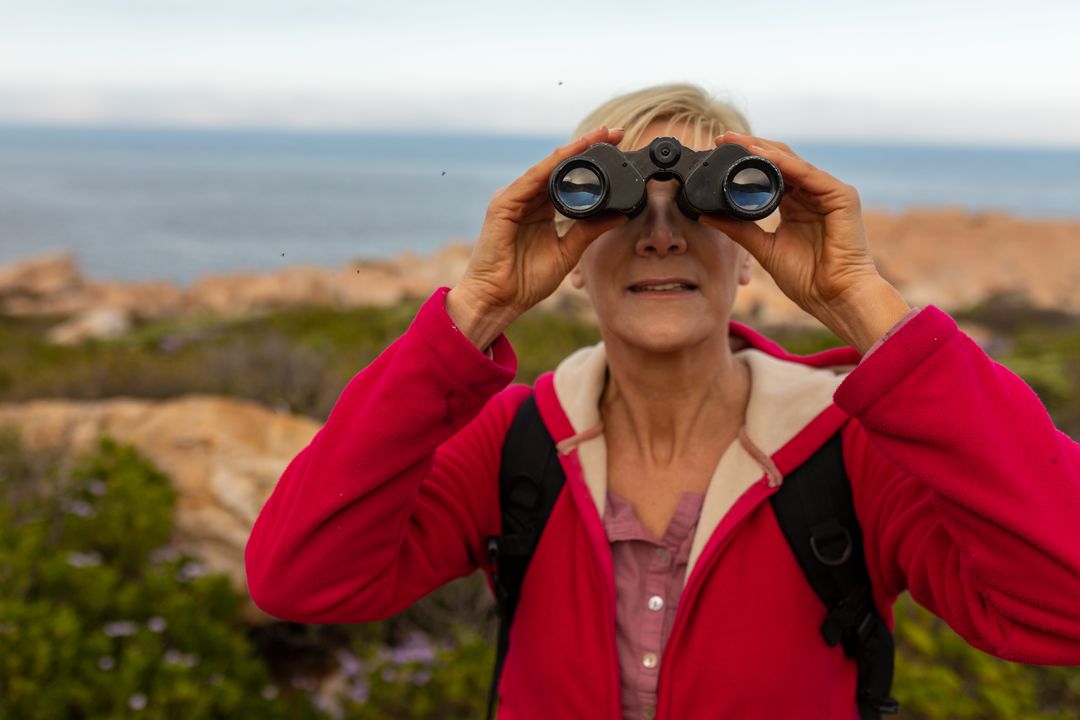 Caucasian hiker senior woman using binoculars while trekking in the mountains - Free Images, Stock Photos and Pictures on Pikwizard.com
