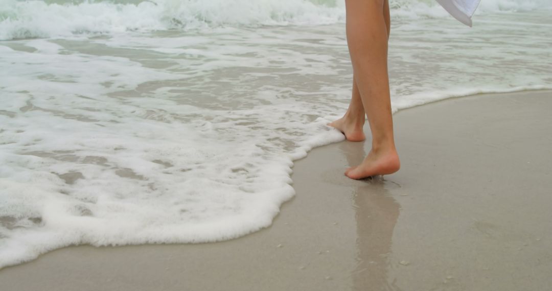 Woman Strolling Barefoot on Sandy Shore With Gentle Sea Foam