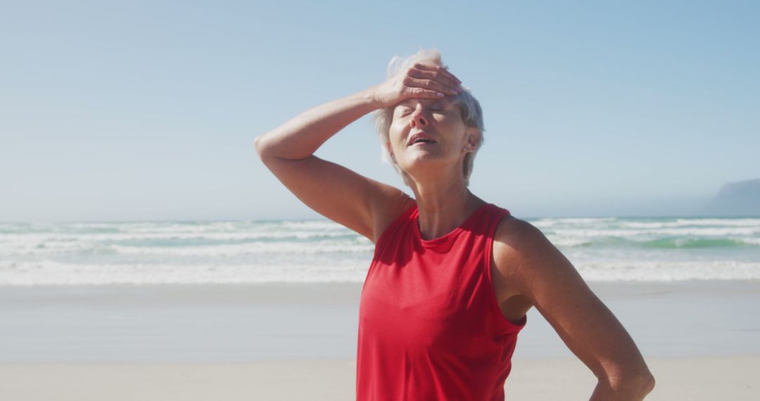 Senior woman in red tank top feeling warm by beach with ocean waves in background - Free Images, Stock Photos and Pictures on Pikwizard.com