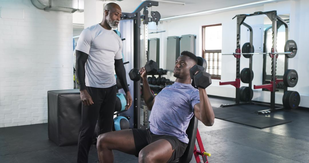 Personal Trainer Guiding Client Lifting Dumbbells in Gym