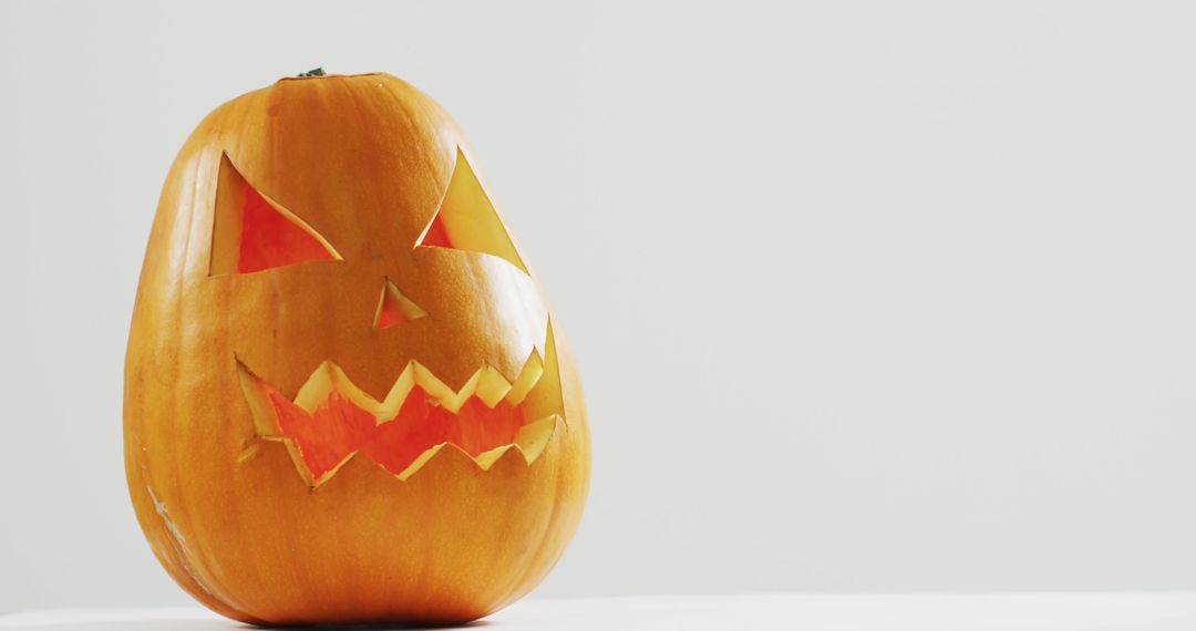 Carved Halloween Pumpkin with Illuminated Face on Light Background - Free Images, Stock Photos and Pictures on Pikwizard.com