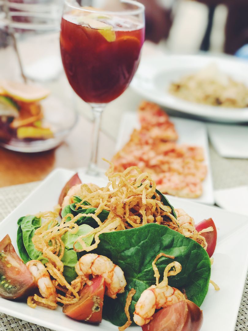 Serving Shrimp Salad with Crispy Fried Onions, Spinach and Tomatoes on Bistro Table