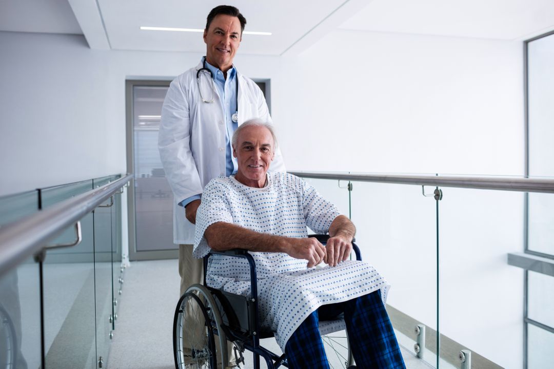 Doctor Smiling with Senior Patient in Wheelchair in Hospital Corridor - Free Images, Stock Photos and Pictures on Pikwizard.com