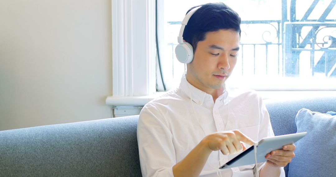 Young Man Relaxing with Music and Tablet by Window