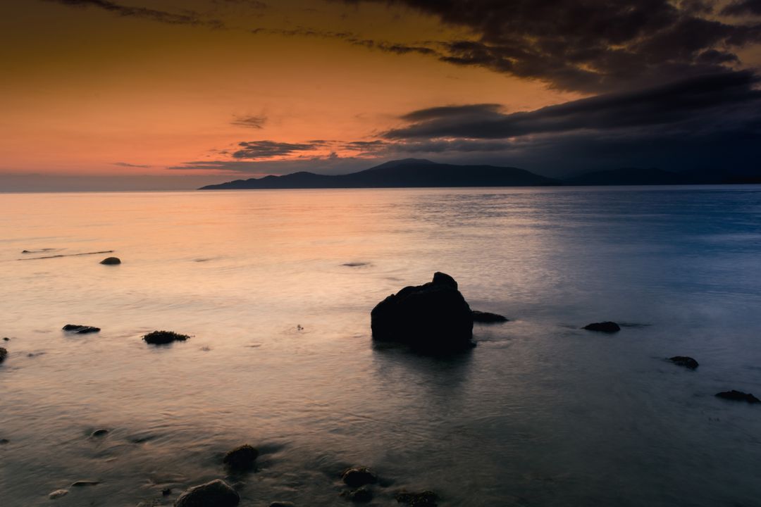 Serene Sunset Over Calm Ocean with Silhouette of Rocks - Free Images, Stock Photos and Pictures on Pikwizard.com
