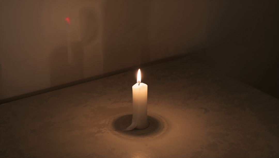 Burning white pillar candle casting warm glow and forming wax ring on patterned table