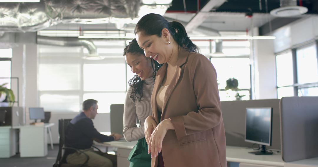 Multicultural women collaborating and smiling in modern open-plan office with monitors