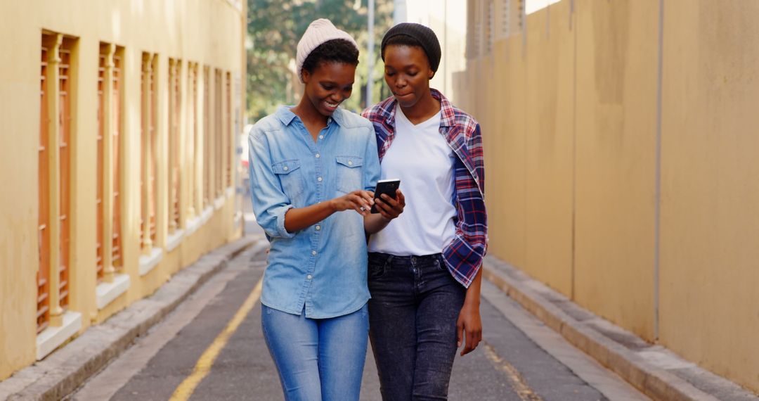 Smiling African American Twin Sisters Using Smartphone Walking City