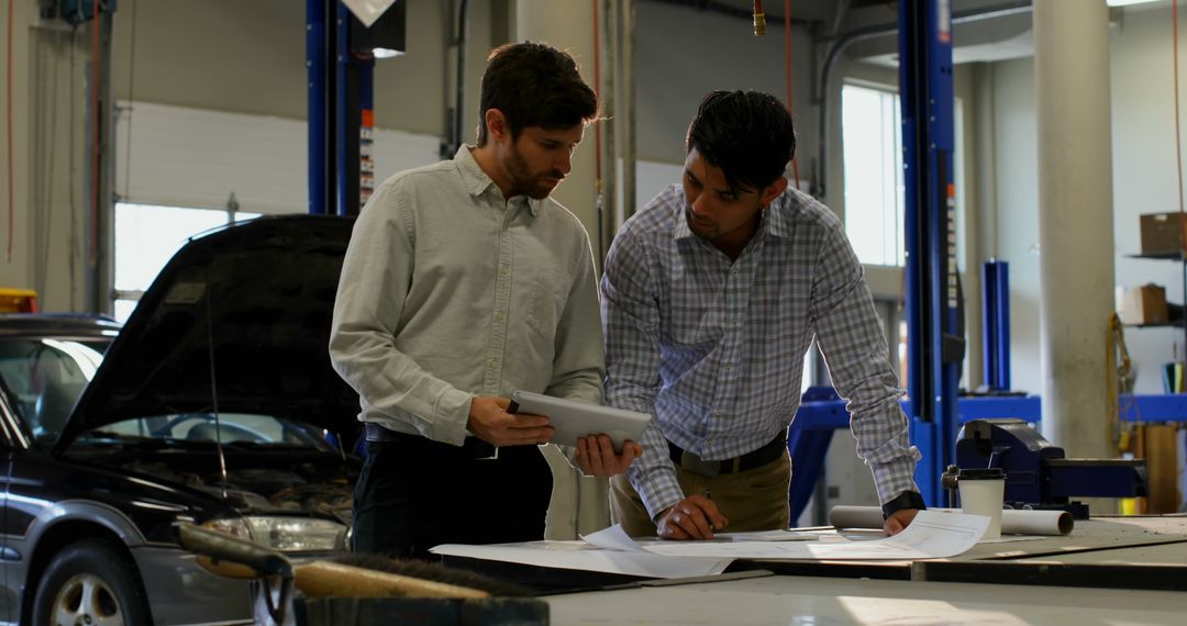 Engineers Discussing Blueprint in Automotive Workshop - Free Images, Stock Photos and Pictures on Pikwizard.com