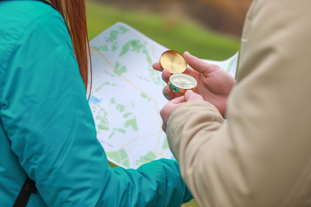 Hikers navigating with compass and paper map outdoors, planning route on nature hike