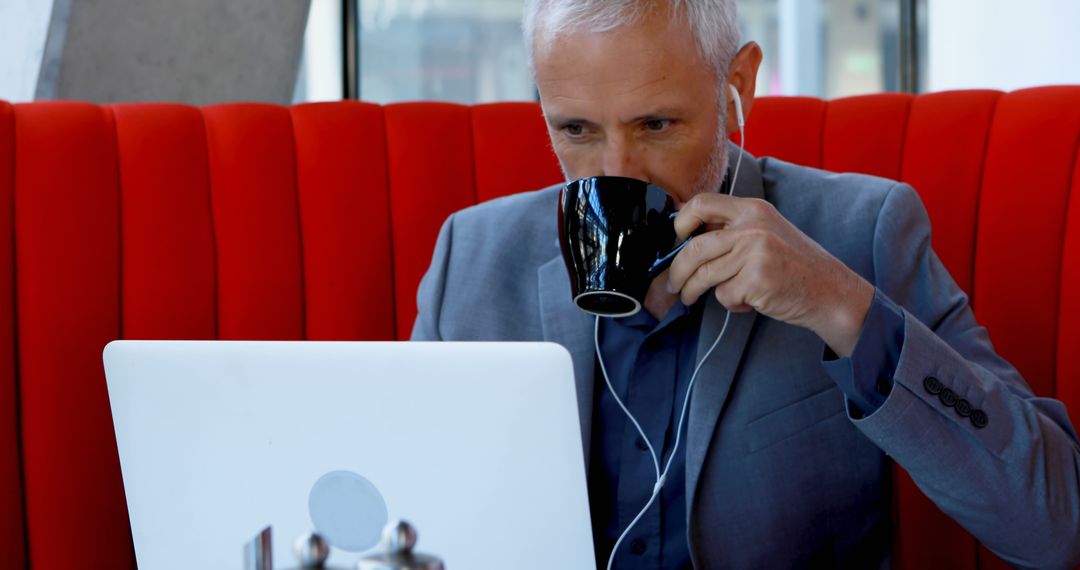 Senior Businessman Drinking Coffee and Working on Laptop in Modern Office - Free Images, Stock Photos and Pictures on Pikwizard.com