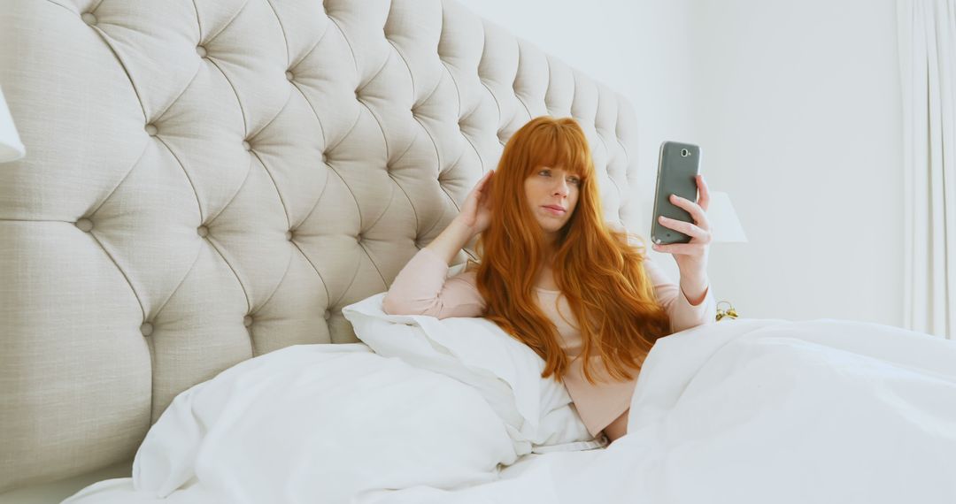 Woman with Red Hair Sitting Up in Bed Looking at Smartphone - Free Images, Stock Photos and Pictures on Pikwizard.com