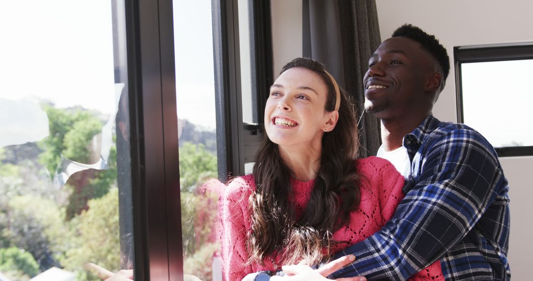 Joyful Diverse Couple Embracing and Smiling by Window