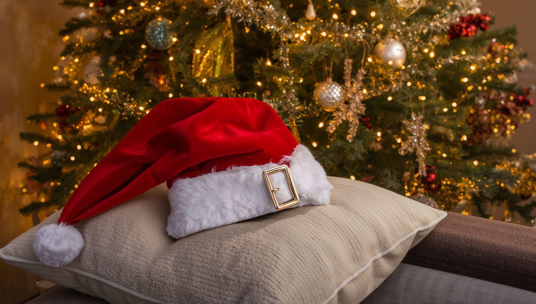 Santa hat resting on beige cushion with gold buckle and glowing Christmas tree lights