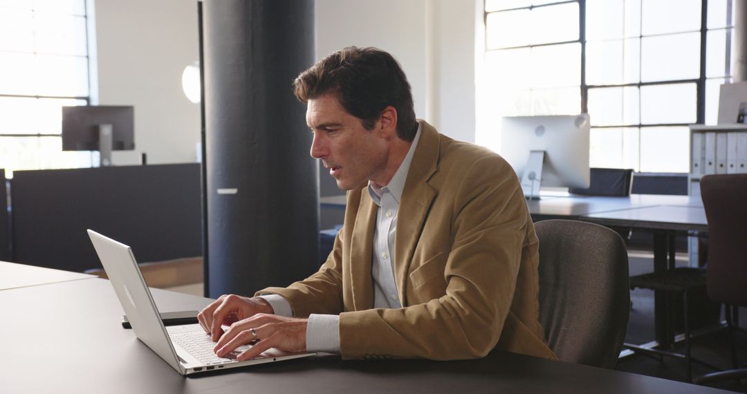 Focused Businessman Typing on Laptop in Modern Office Setting