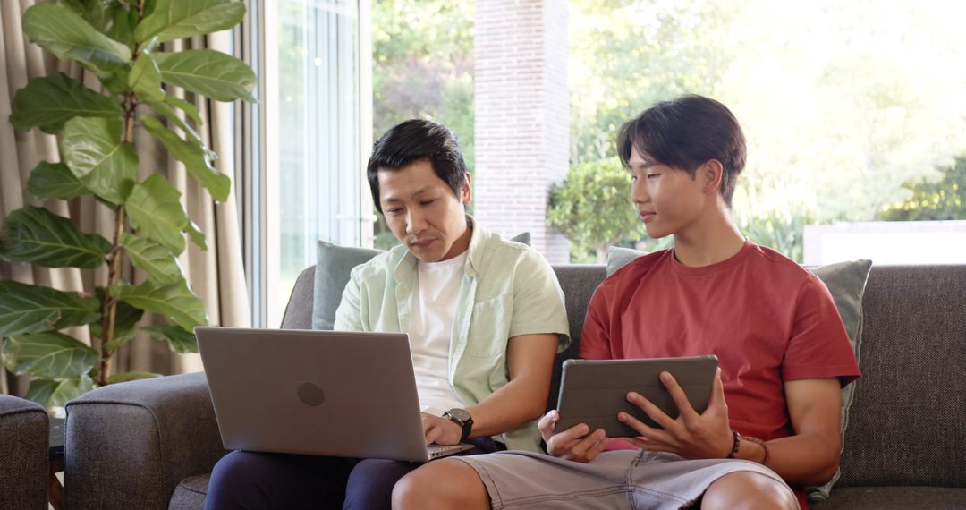 Father and Son Using Laptop and Tablet on Cozy Couch