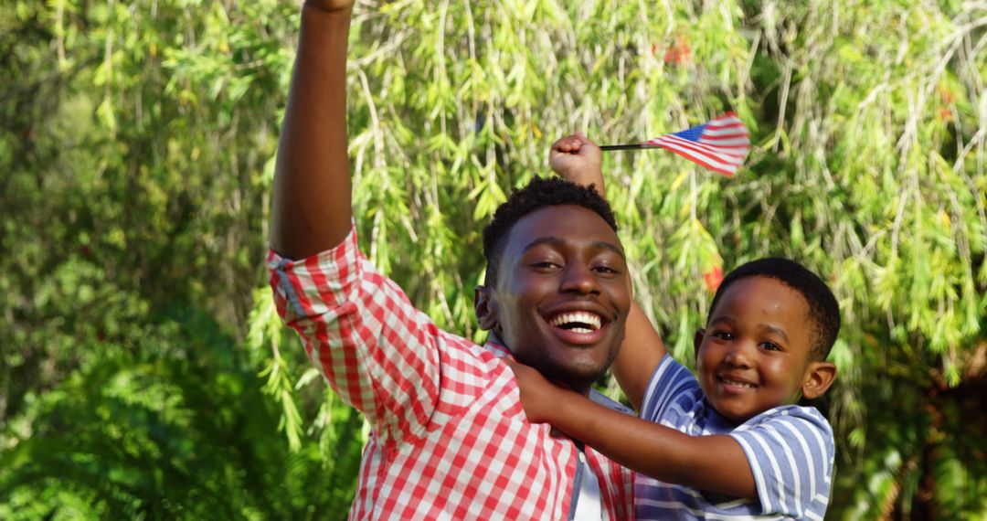 Happy African American Father and Son Celebrating Outdoors with Flag - Free Images, Stock Photos and Pictures on Pikwizard.com