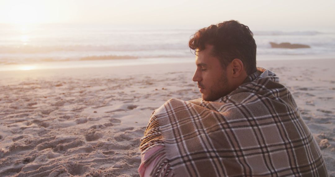 Contemplative Man on Beach Covered in Plaid Blanket During Sunset - Free Images, Stock Photos and Pictures on Pikwizard.com