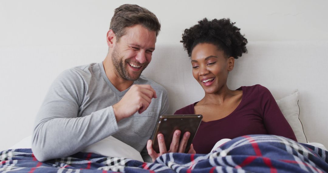 Image of happy diverse couple using tablet in bed and talking - Free Images, Stock Photos and Pictures on Pikwizard.com