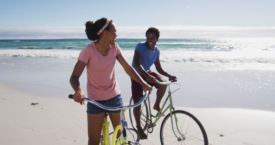 African american couple smiling and riding bikes on the beach - Free Images, Stock Photos and Pictures on Pikwizard.com