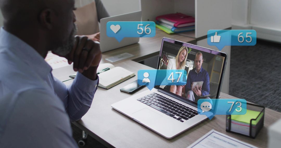 Mature professional watching virtual meeting on laptop with social engagement overlays