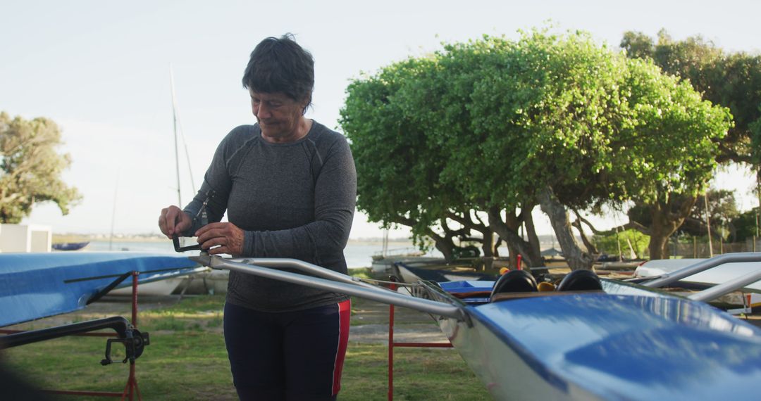 Senior woman preparing rowing boat at sunny lakeside - Free Images, Stock Photos and Pictures on Pikwizard.com