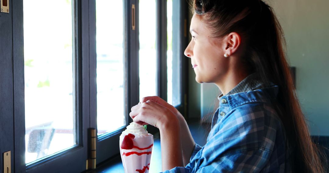 Woman enjoying strawberry milkshake by window - Free Images, Stock Photos and Pictures on Pikwizard.com