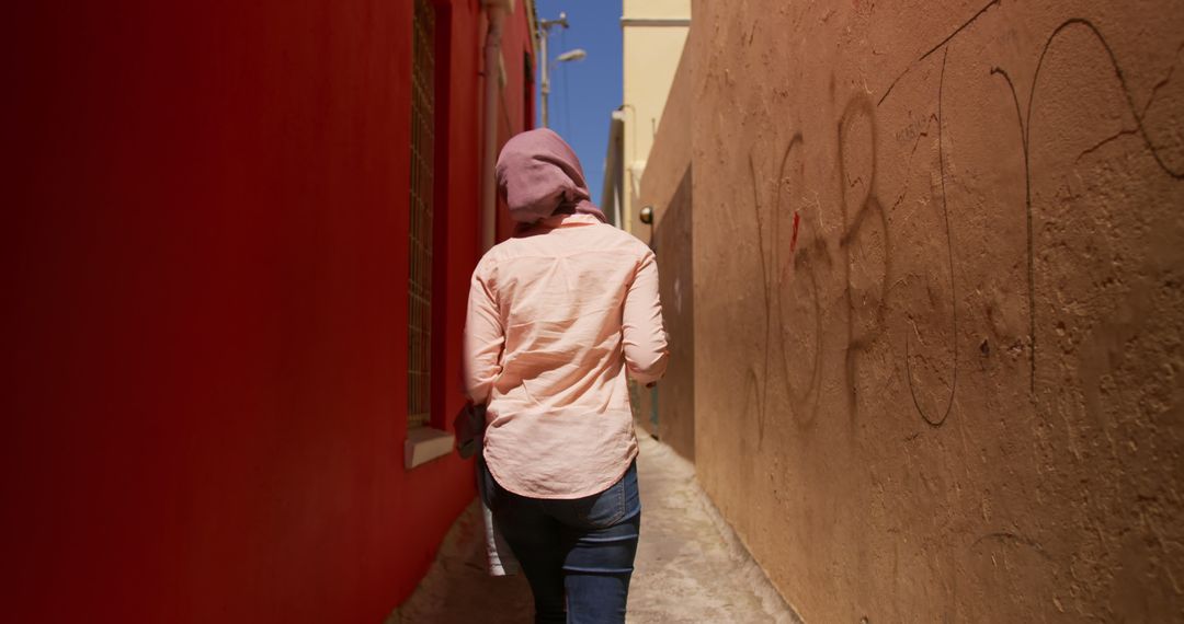 Woman Walking in Narrow Alley Between Red and Beige Walls on a Sunny Day - Free Images, Stock Photos and Pictures on Pikwizard.com