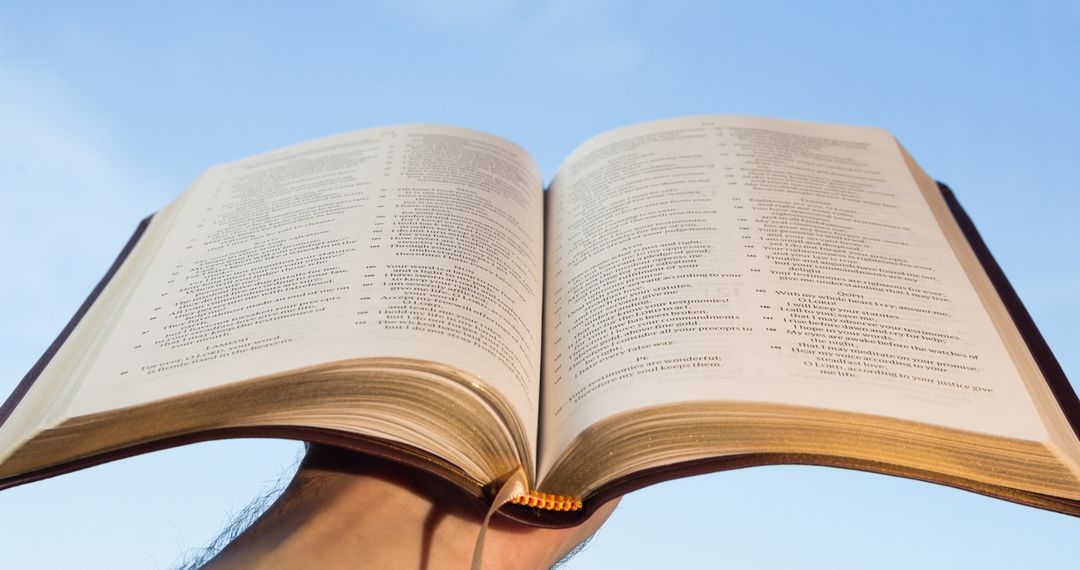 Hands Holding Open Bible Against Clear Sky for Easter Reflection