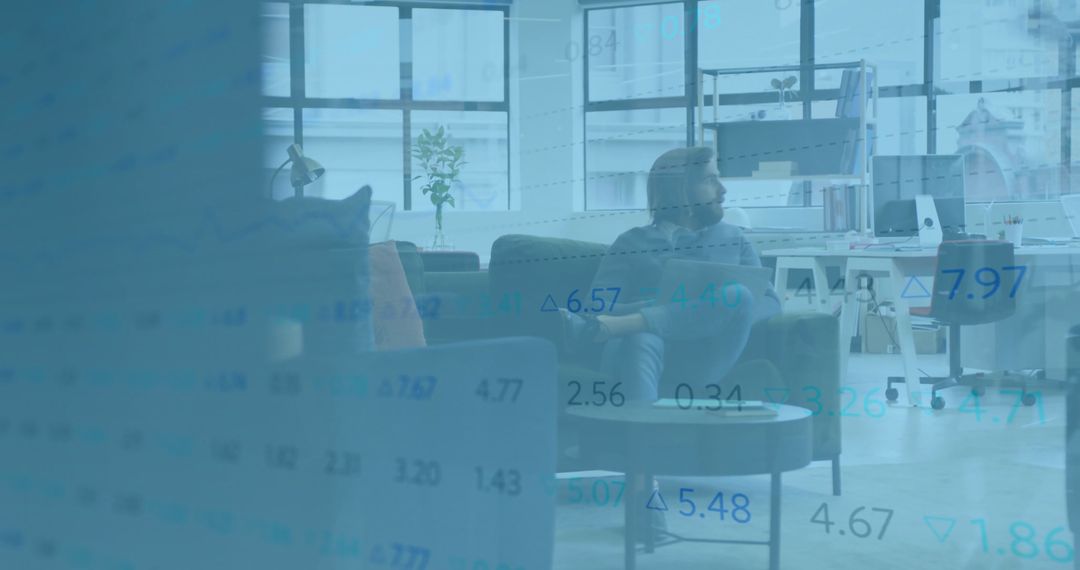Young professional sitting in modern office lounge analyzing financial data overlay