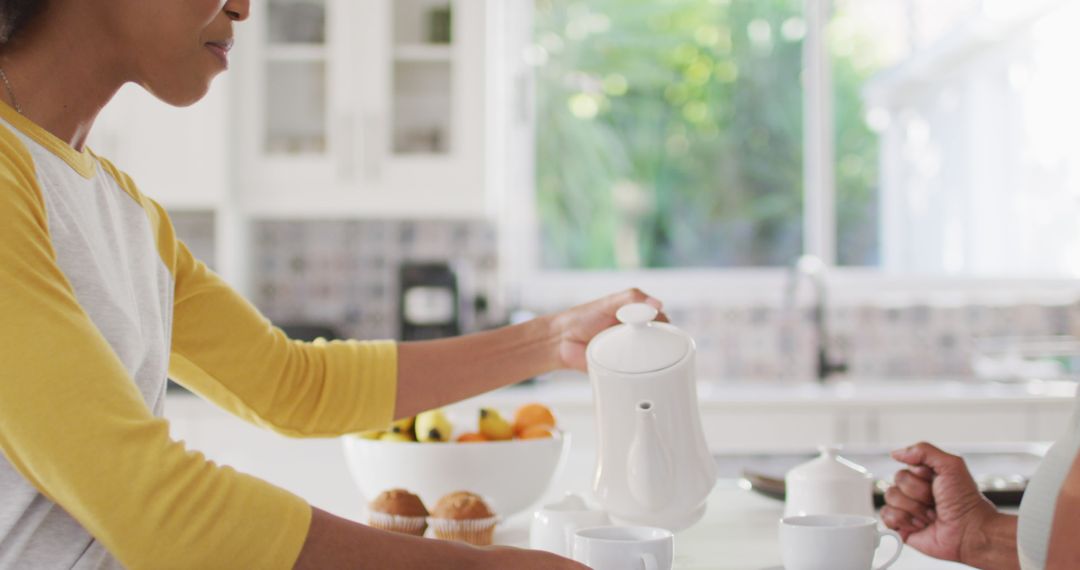 Woman Pouring Tea in Bright Kitchen with Fruit Bowl and Muffins - Free Images, Stock Photos and Pictures on Pikwizard.com