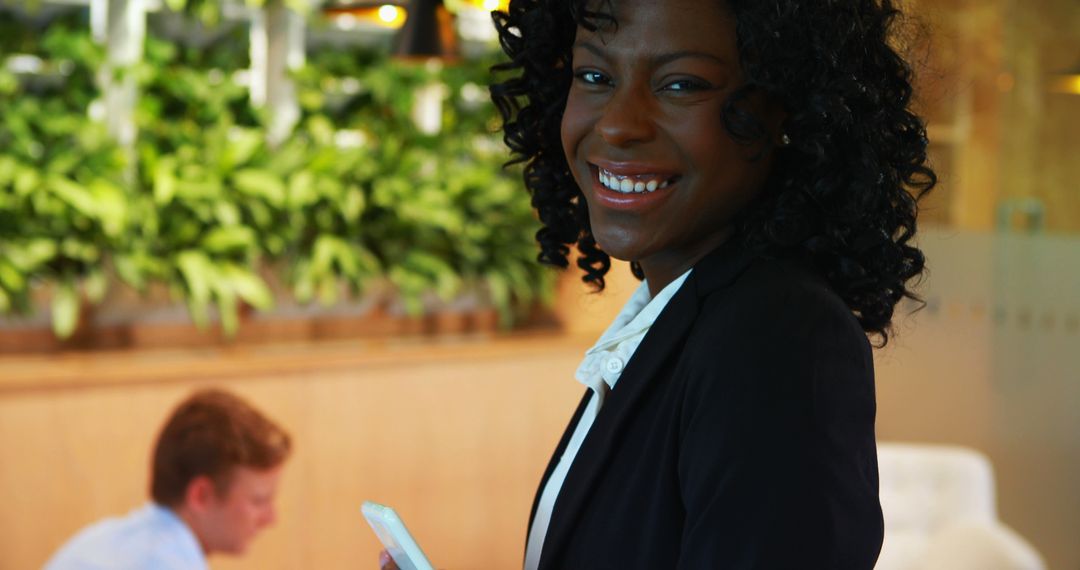 Smiling Businesswoman Holding Smartphone in Office with Colleague - Free Images, Stock Photos and Pictures on Pikwizard.com