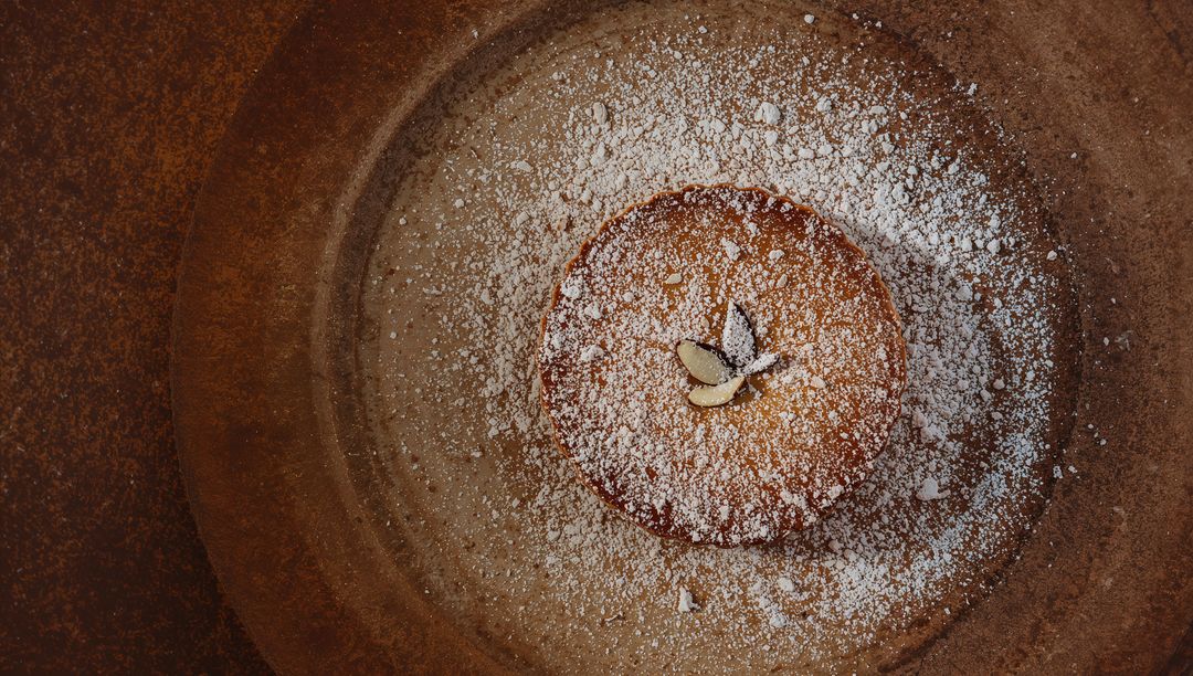 Almond tart sitting on rustic brown plate dusted with powdered sugar