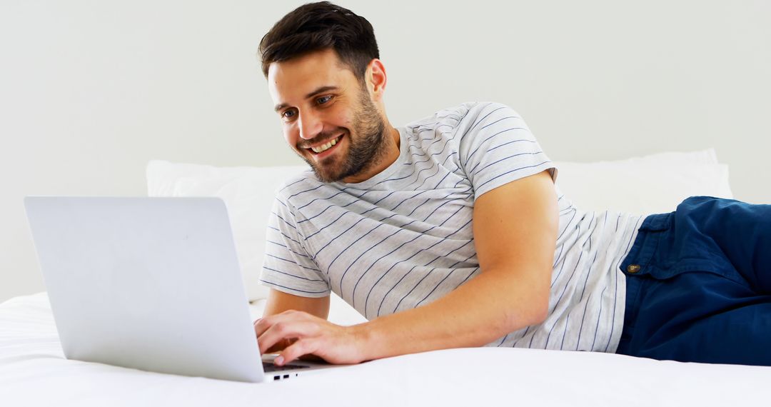 Smiling Man Relaxing on Bed Using Laptop - Free Images, Stock Photos and Pictures on Pikwizard.com