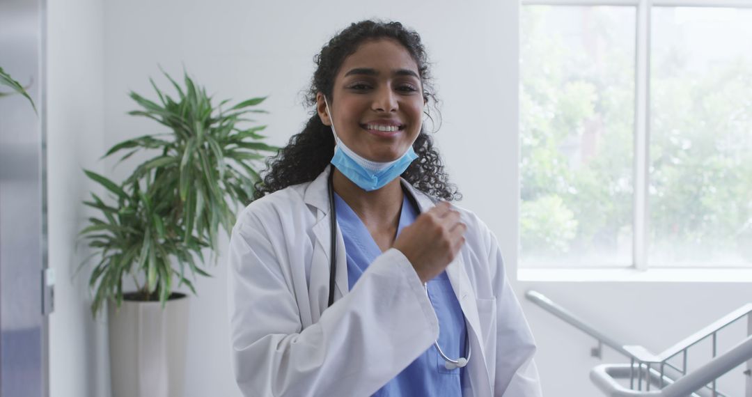 Portrait of asian female doctor lowering face mask and smiling in hospital - Free Images, Stock Photos and Pictures on Pikwizard.com