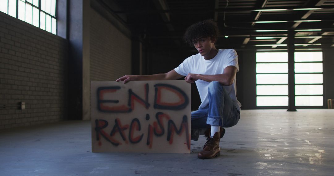 Young Man Holding 'End Racism' Sign in Industrial Space - Free Images, Stock Photos and Pictures on Pikwizard.com