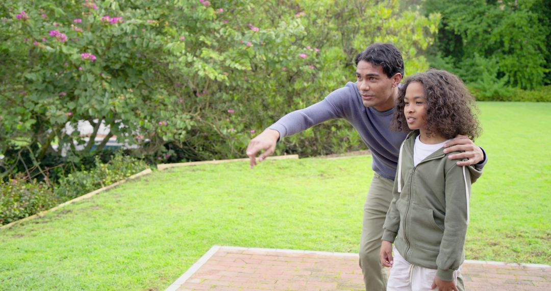 Father pointing and guiding son on brick patio in backyard garden with green lawn