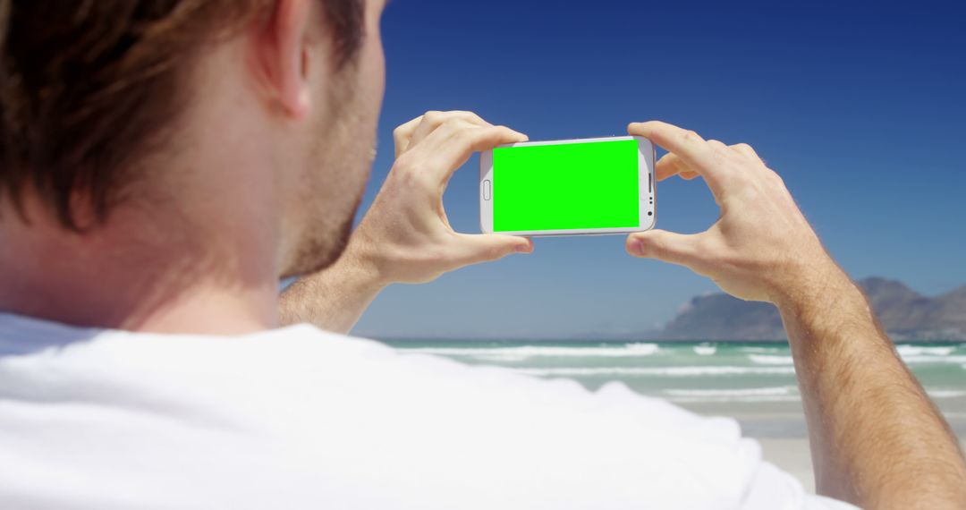 Man Enjoying Beach While Taking Photo on Smartphone with Green Screen - Free Images, Stock Photos and Pictures on Pikwizard.com