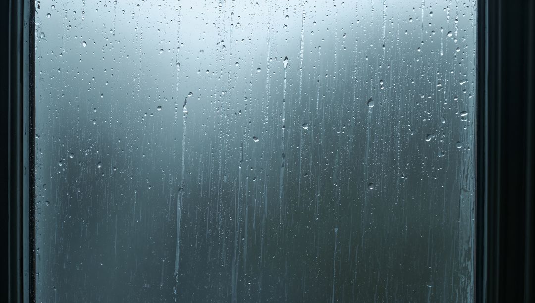 Raindrops Sliding Down Window Glass with Moody Blue Light and Fogged Condensation