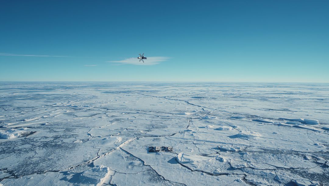 Hovering drone casting shadow over 2023 numerals on polar sea ice horizon