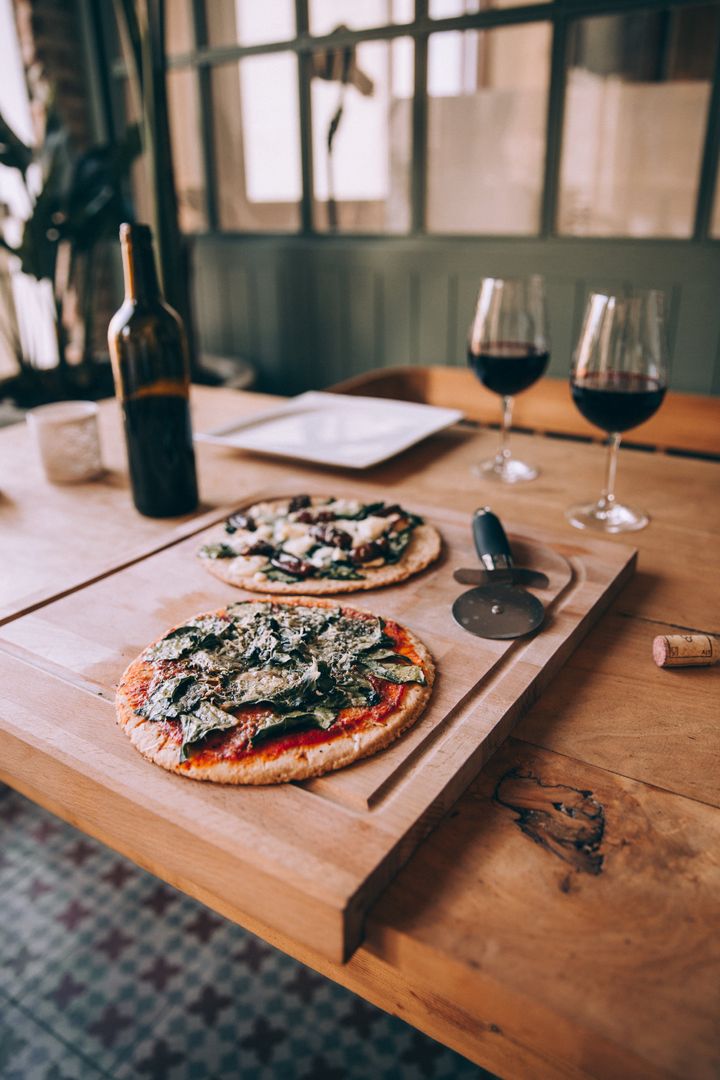 Rustic wooden table serving two artisan thin-crust pizzas with red wine for two