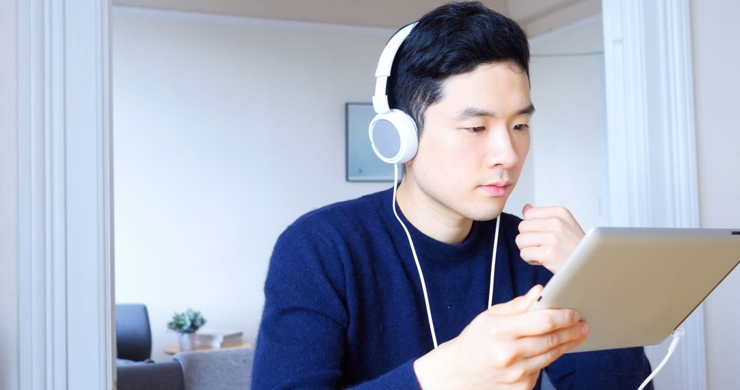 Focused Man Wearing Headphones Using Tablet at Home - Free Images, Stock Photos and Pictures on Pikwizard.com