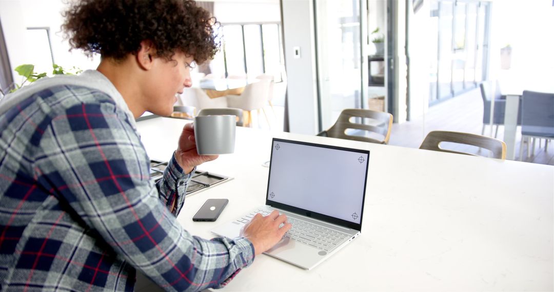 Man Balancing Coffee While Working on Laptop in Modern Kitchen