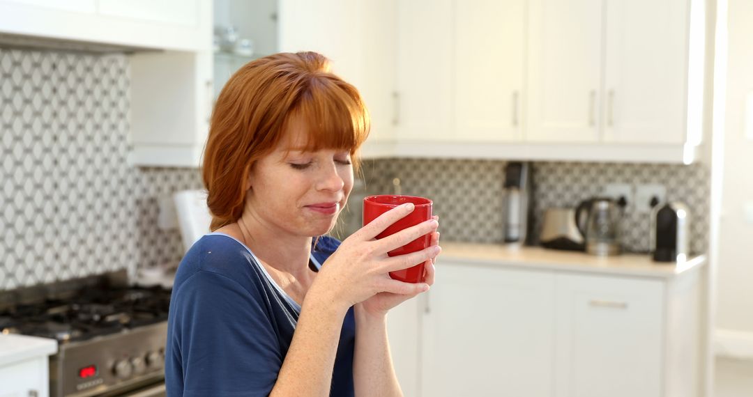 Woman with red hair enjoying hot beverage in modern kitchen - Free Images, Stock Photos and Pictures on Pikwizard.com